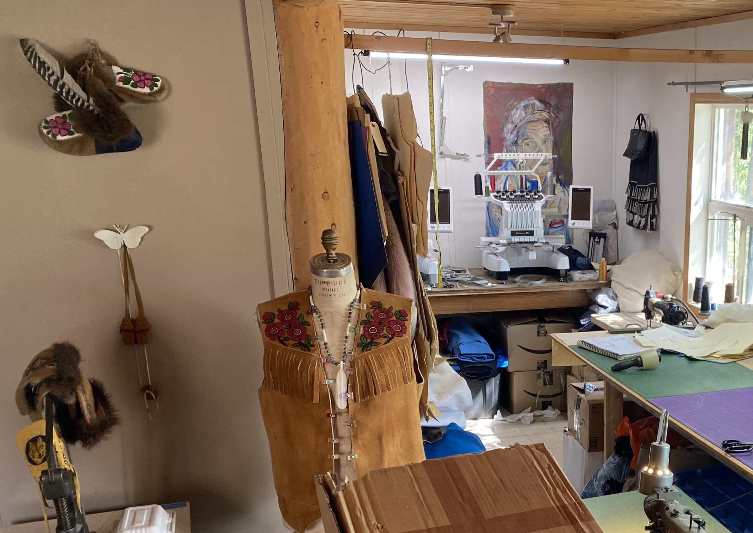 Beaded moosehide vest on a form in the Enterprise studio, embroidery machine and cutting table behind it