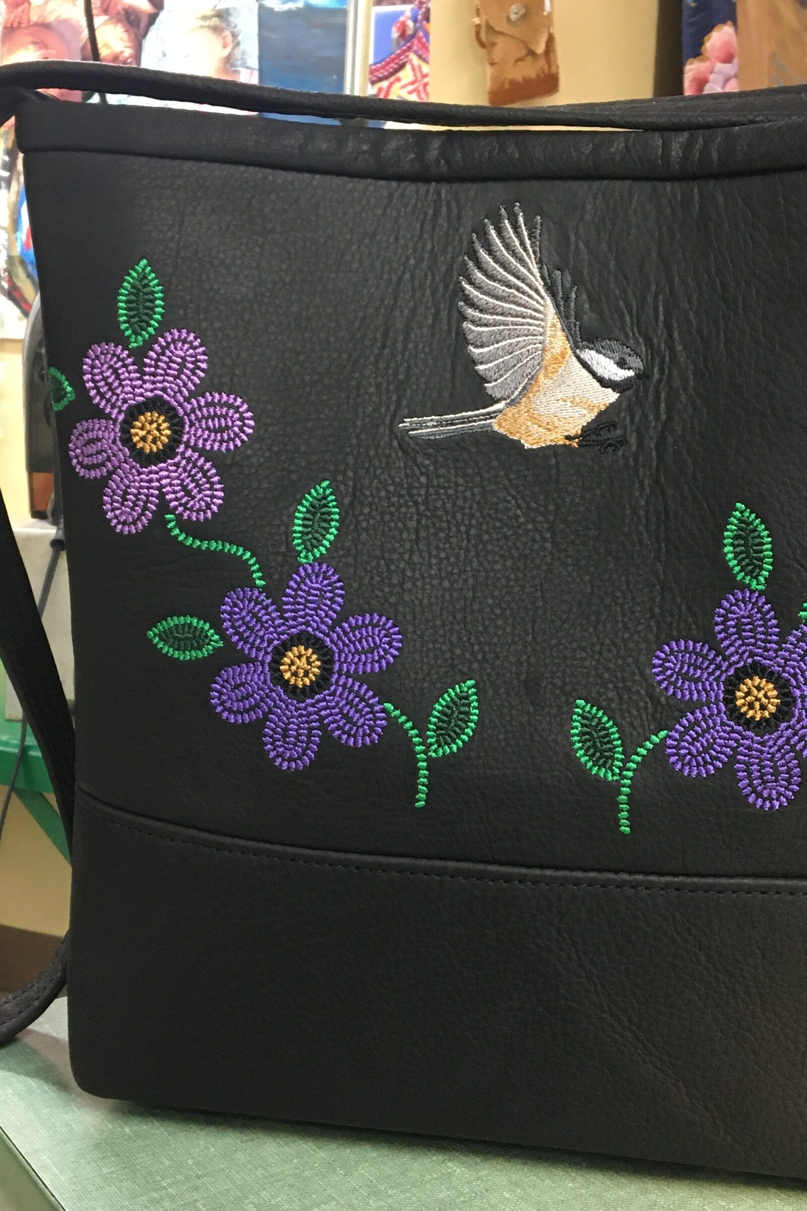 Black leather bag with purple beaded flowers and a chickadee in flight.