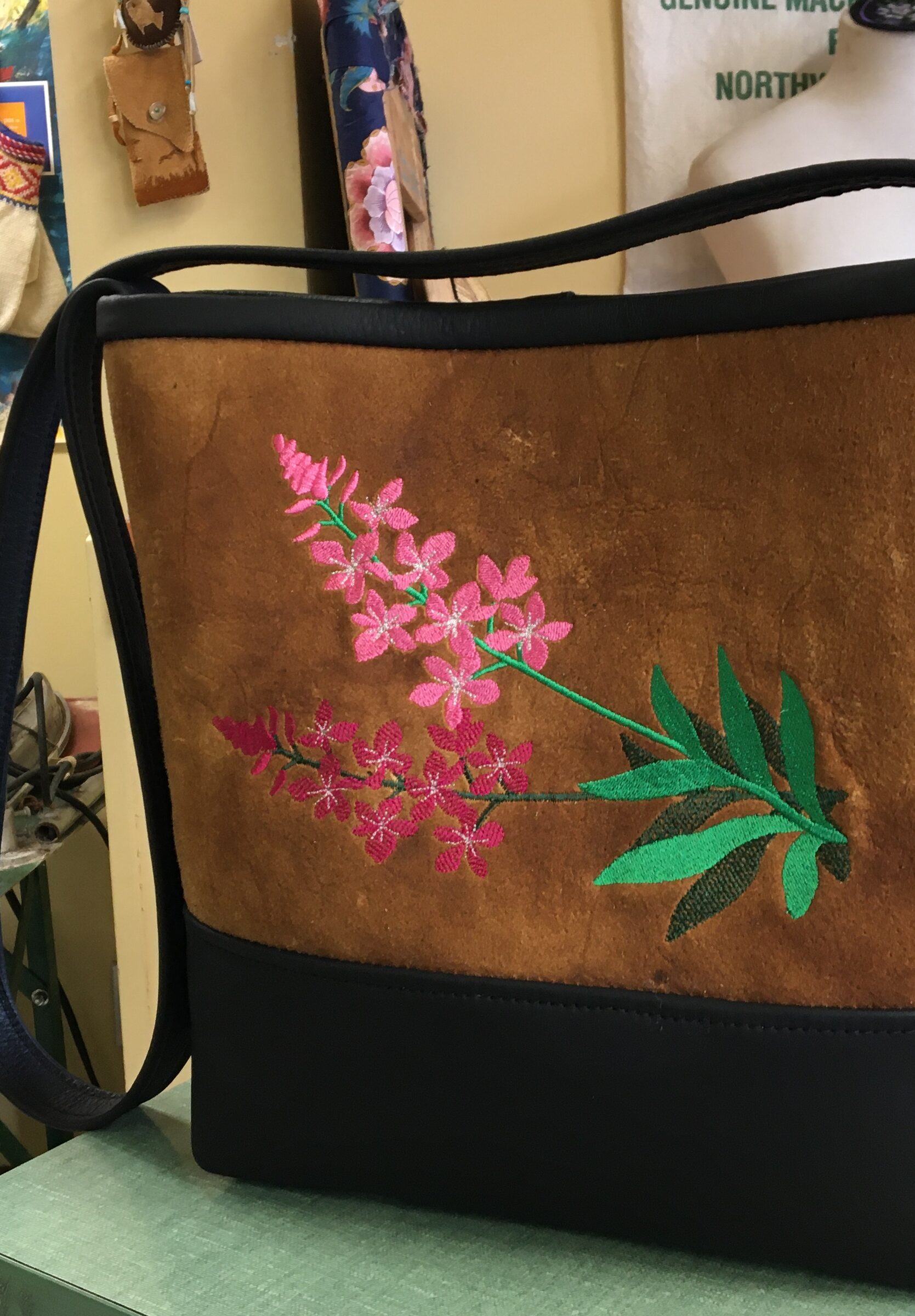 Tan hide shoulder bag with black leather trim and a pink fireweed embroidery.