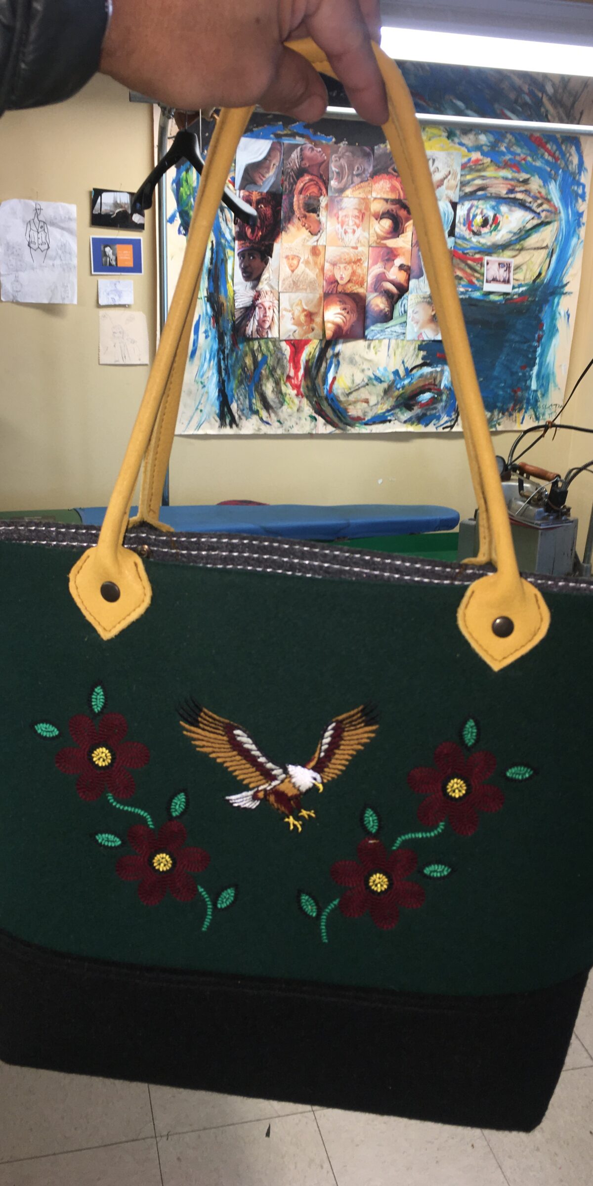 Green felt tote with an embroidered eagle and yellow straps, held up in the studio
