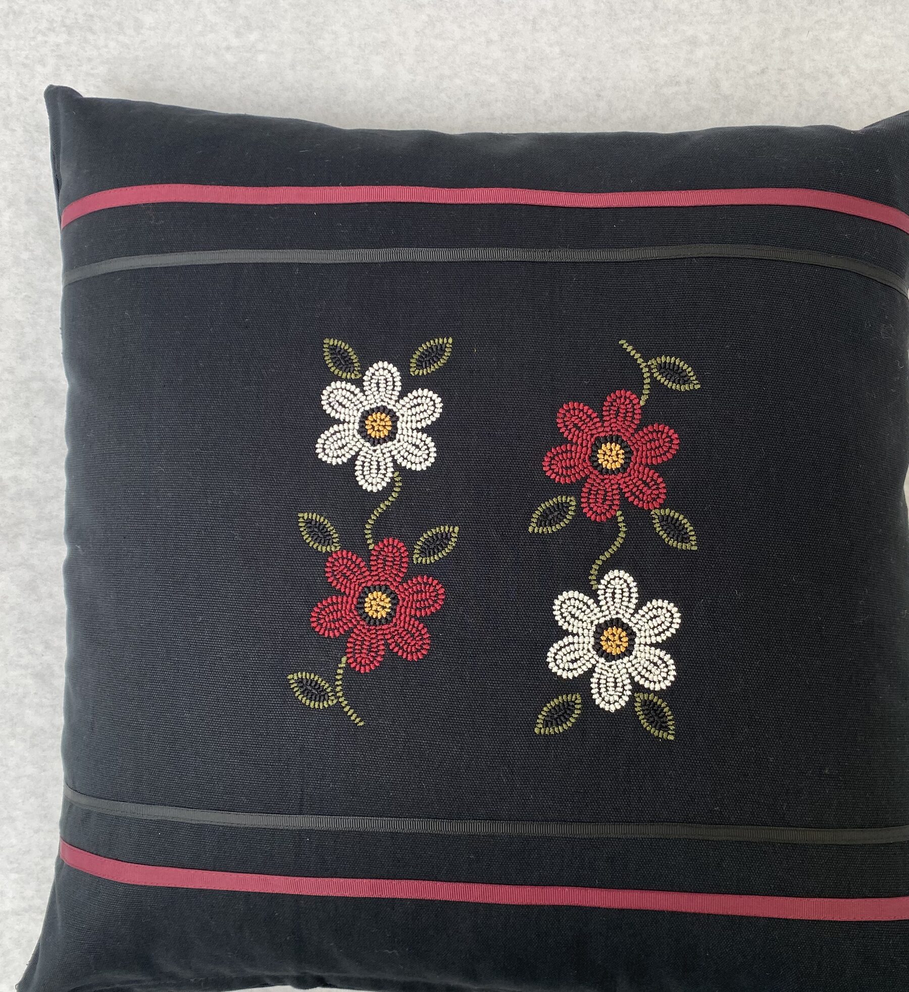 Black pillow with four seed-bead flowers, red and white, on a dark field.