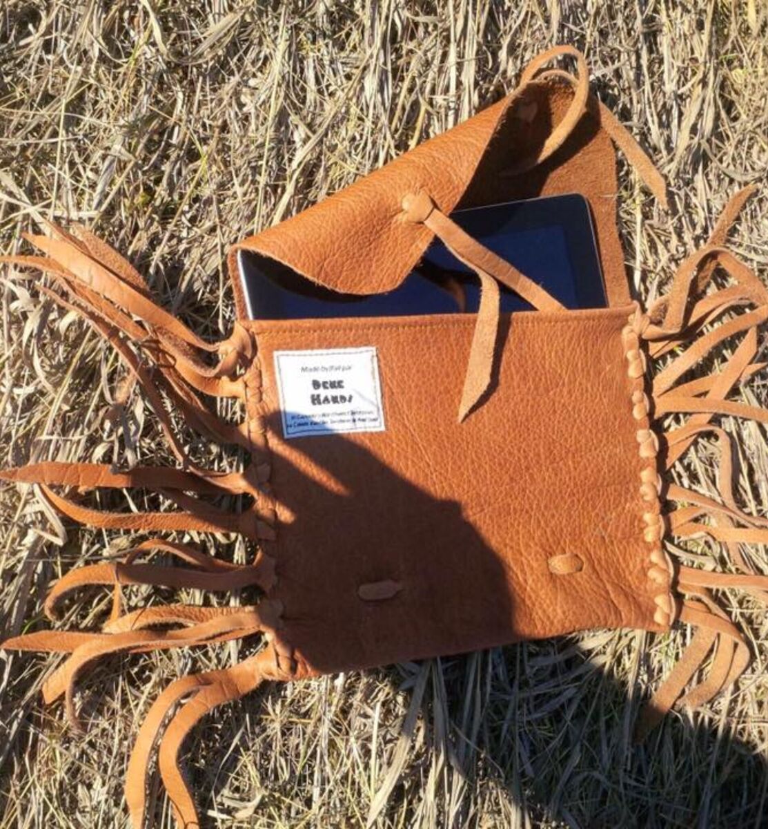 Fringed moosehide sleeve holding a tablet, on dry grass