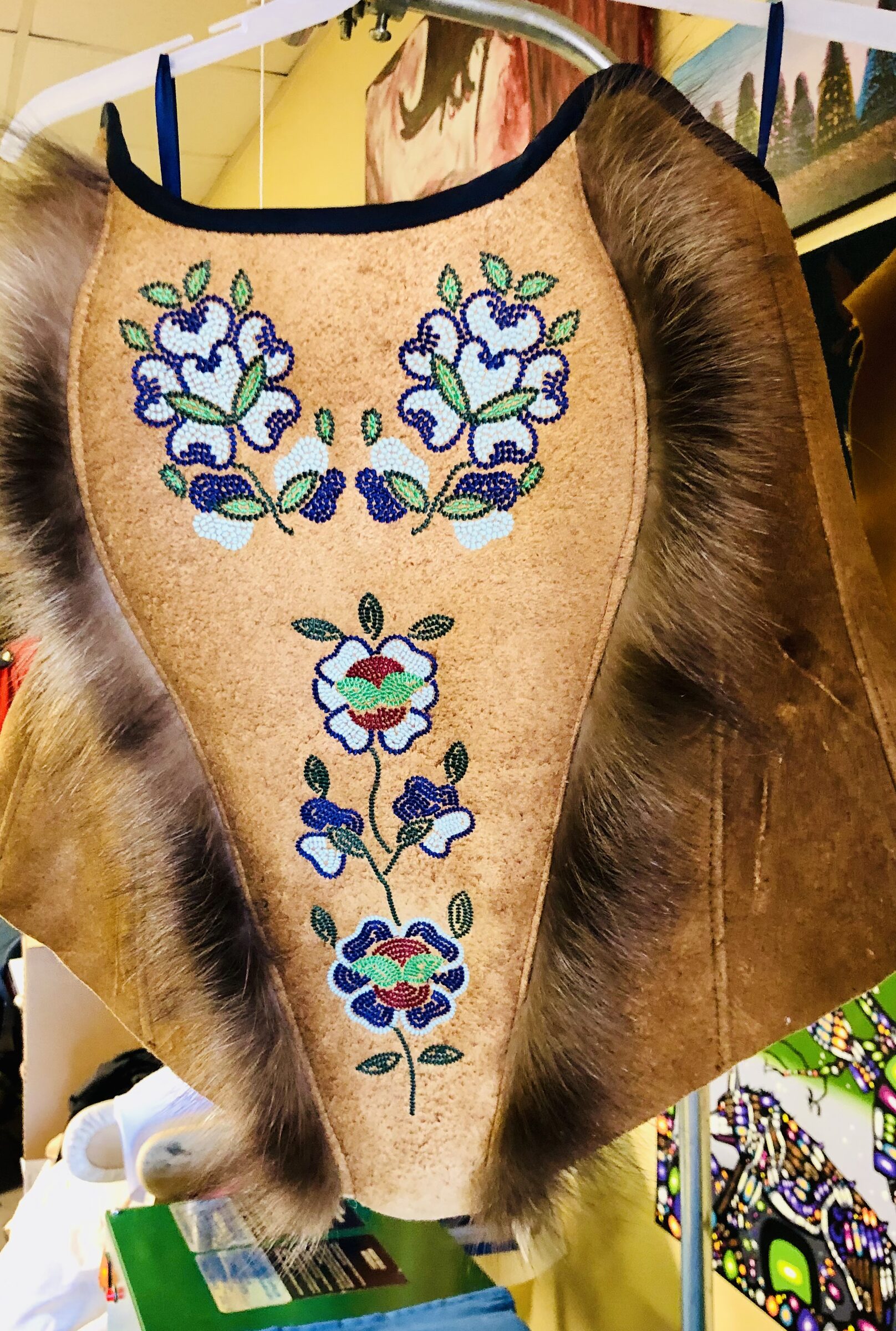 Beaded hide vest with floral work and fur, hanging in the studio